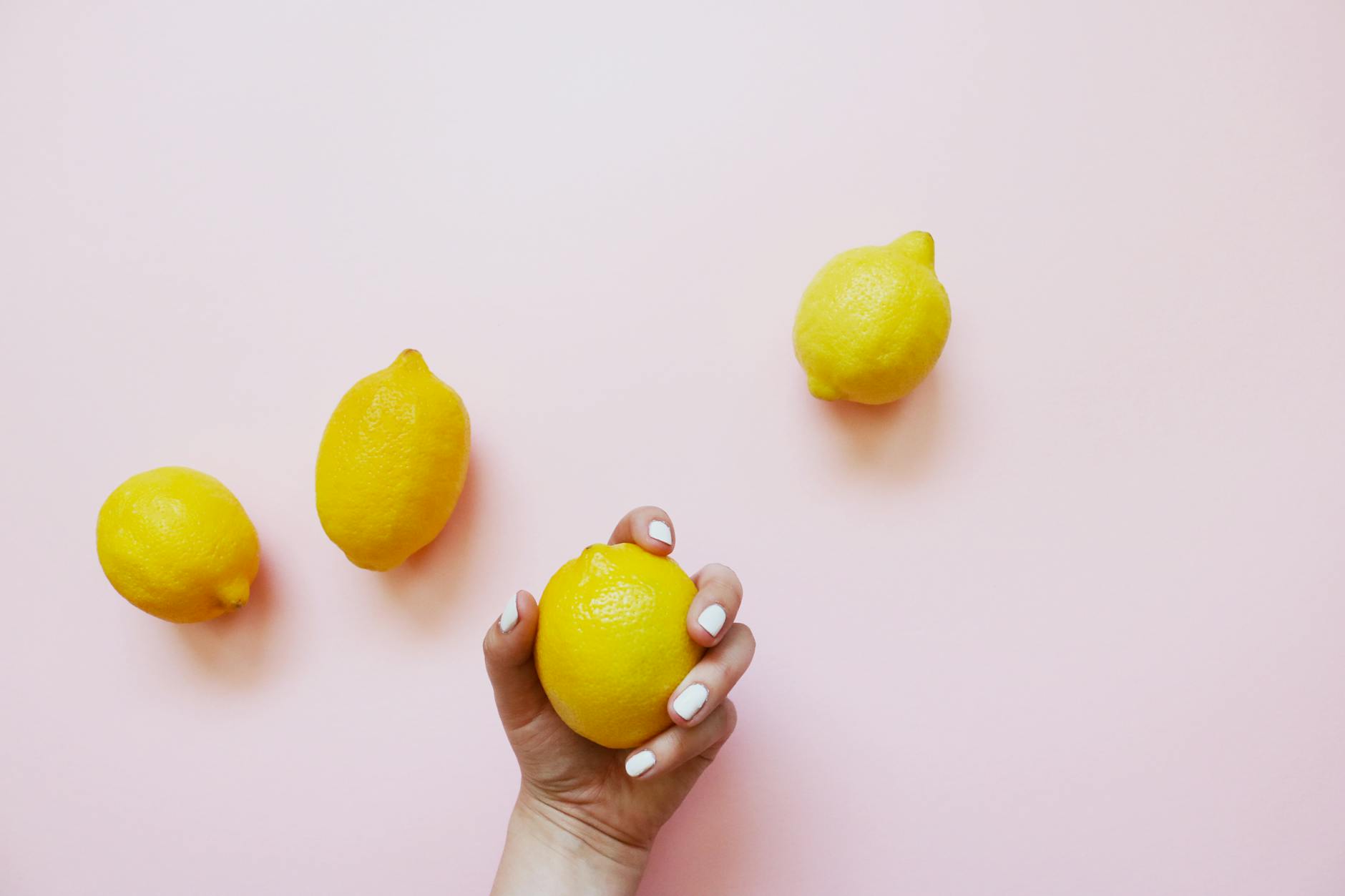 A hand holding a lemon on soft pink background, symbolizing gentle wellness and recovery