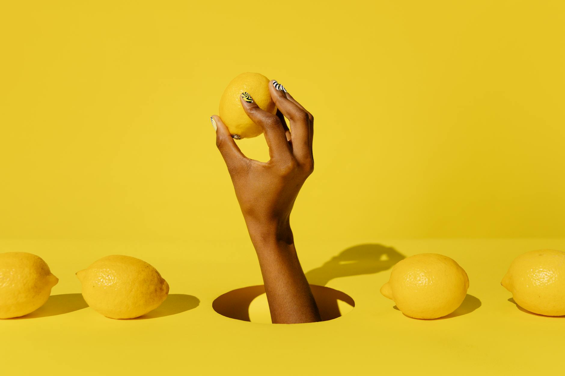 A hand holding a lemon against a vivid yellow background, symbolizing fresh sensuality and vitality