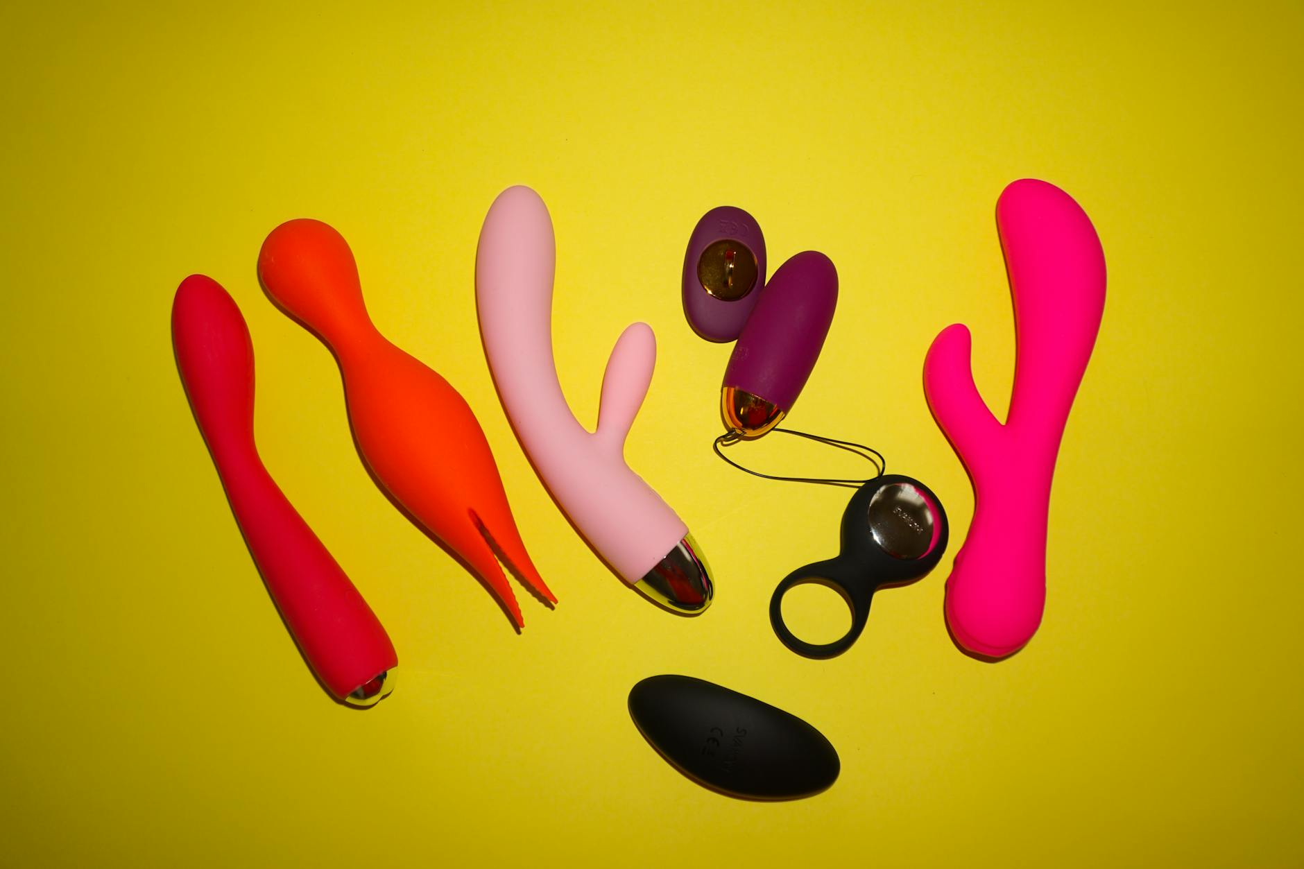 Studio setup showcasing colorful sex toys on a bright yellow background featuring various shapes and designs.